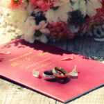 Close-Up Of Wedding Rings On Red Book Over Table